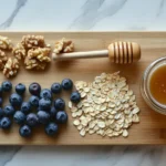 Wooden cutting board with rolled oats, blueberries, walnuts, honey, almond milk, and cinnamon.