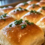 Close-up of golden and fluffy cottage cheese bread rolls, garnished with fresh parsley on a rustic wooden table.